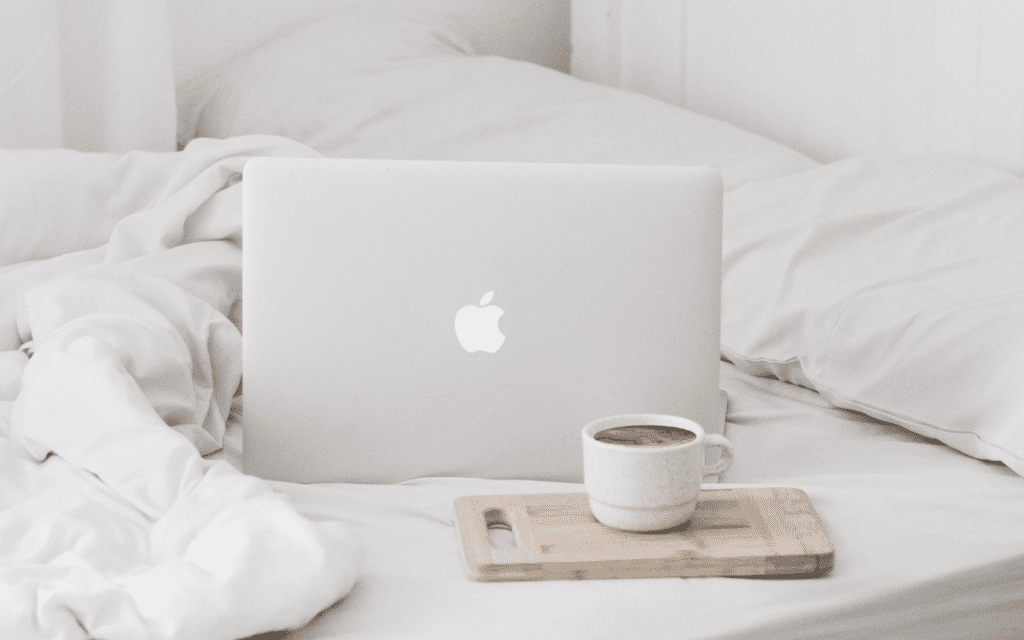Apple laptop and coffee sitting on a bed.