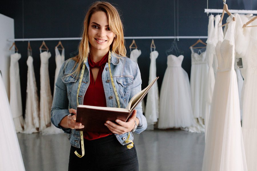bridal store employee with notebook surrounded by bridal dresses